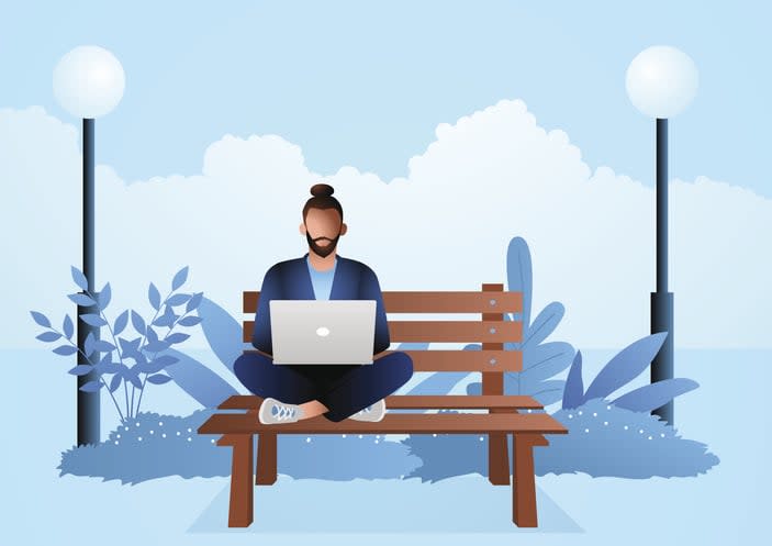 Young man sitting on wooden bench in the park while working with laptop